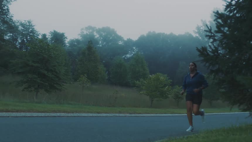 A woman jogging on an empty street surrounded by trees on a misty morning