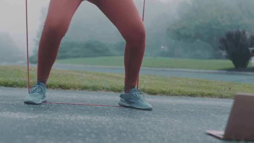 Person following a routine on a laptop exercises with exercise bands outdoors on a foggy day