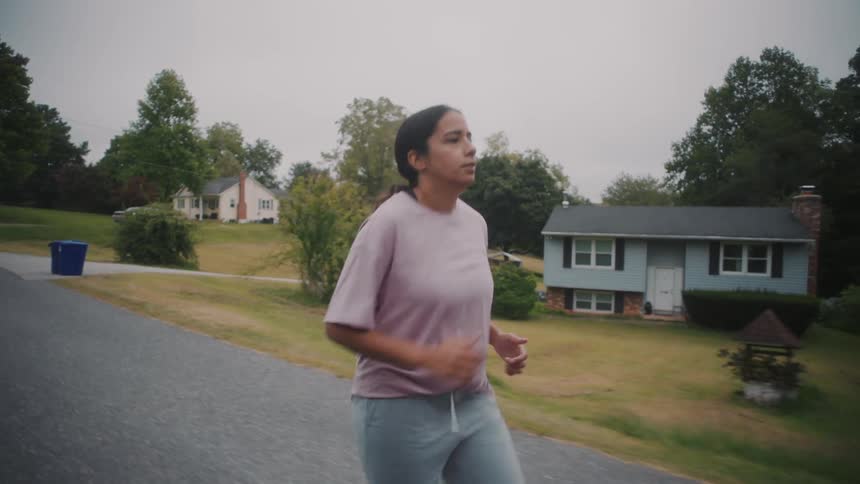 A woman jogging on an empty street surrounded by trees in the morning