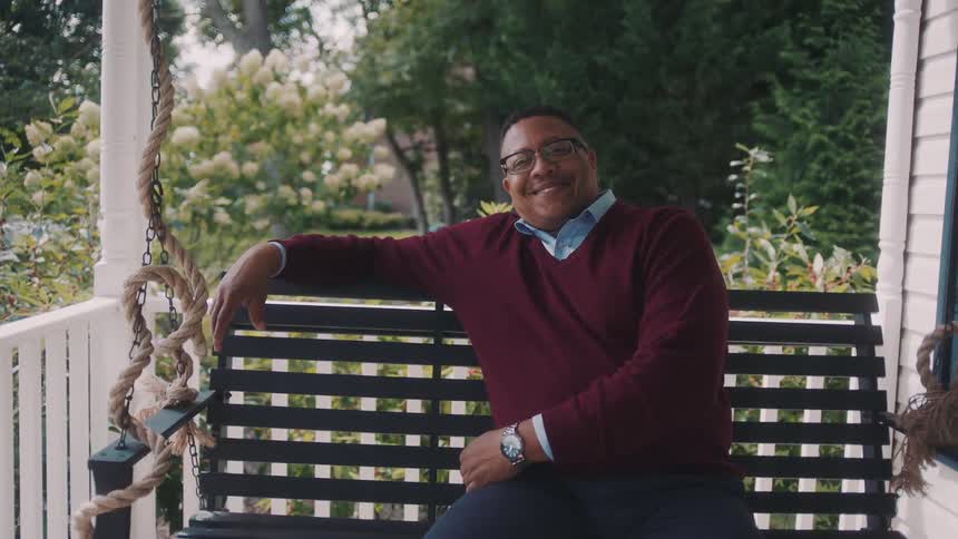 Man with happy facial expression sitting on a bench in an outdoor area of the house