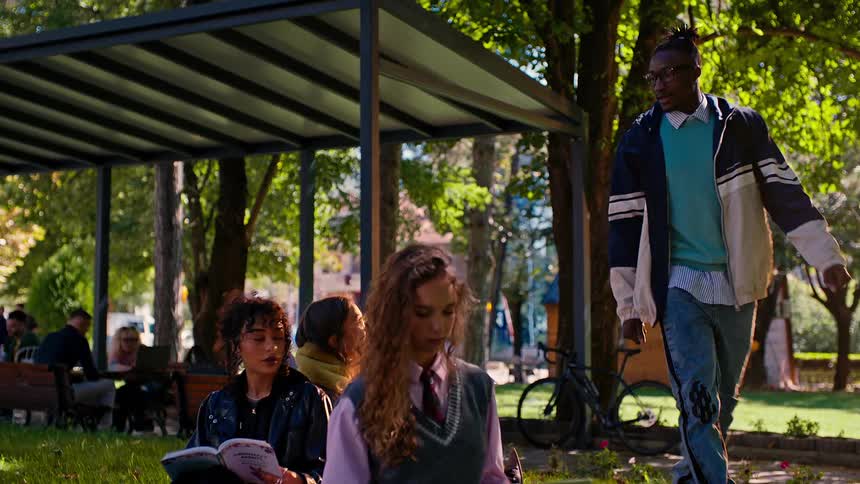 A black man walks up to a group of girls sitting on a blanket in a park and sits down to talk to them