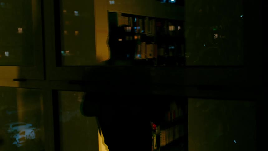 Man carries books through the library passing a reflective window at night