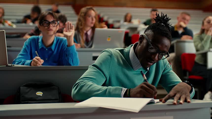 College students in classroom writing and raising hands