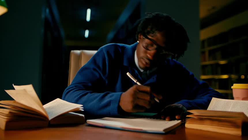 A student reads books and takes notes in a library at night