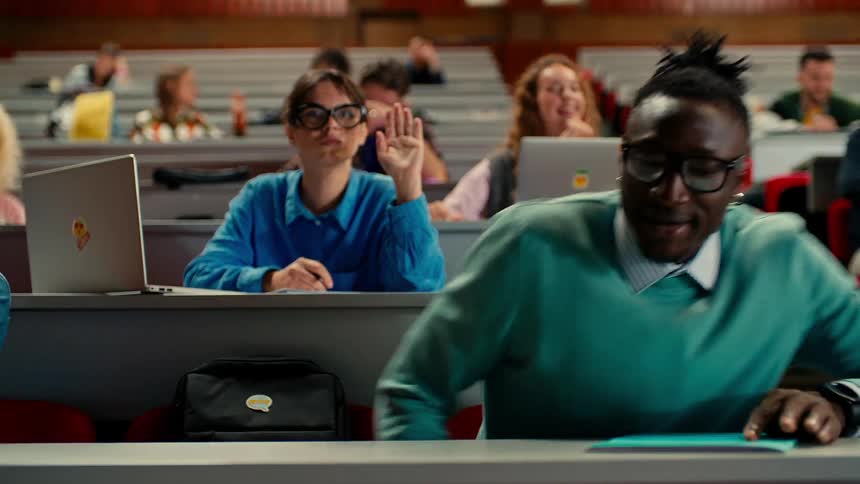 A college student arrives late to a class where others are working on laptops and raising their hands