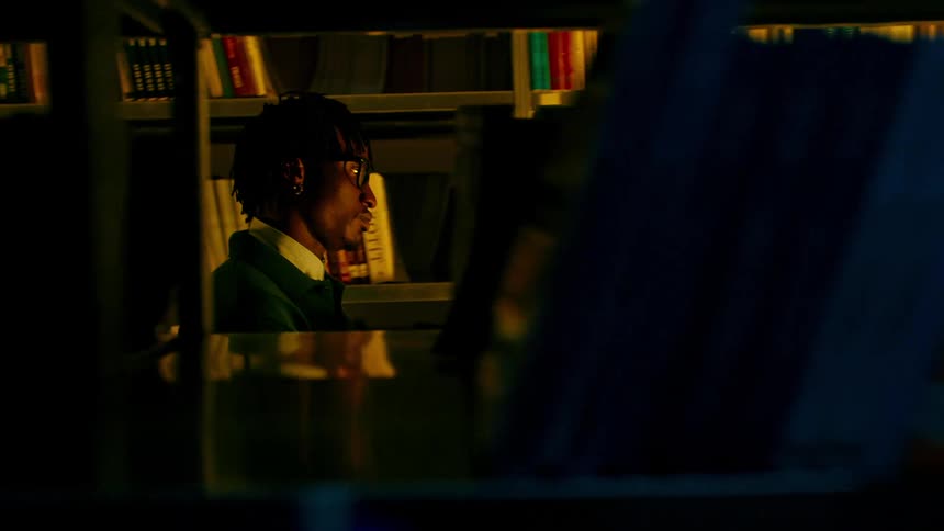 A black student takes books off of a library shelf and walks off with them