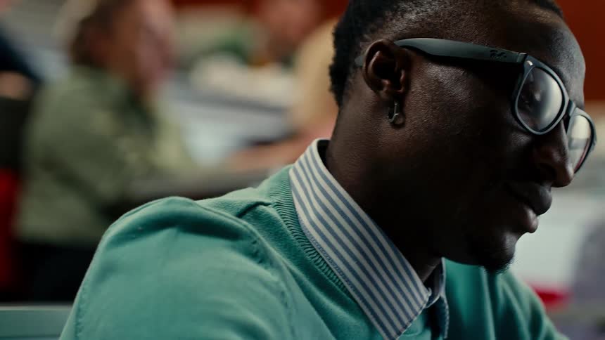 A young man wearing glasses and a green sweater attends a college class