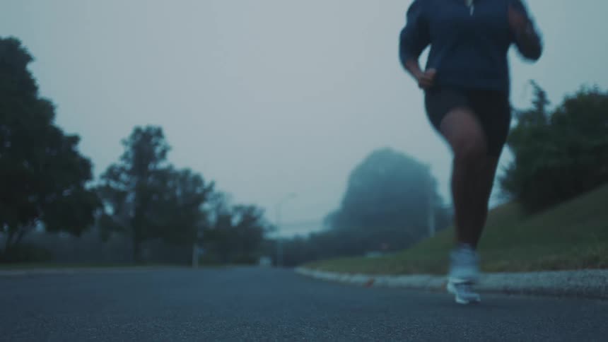 A woman jogging on an empty street surrounded by trees on a misty morning