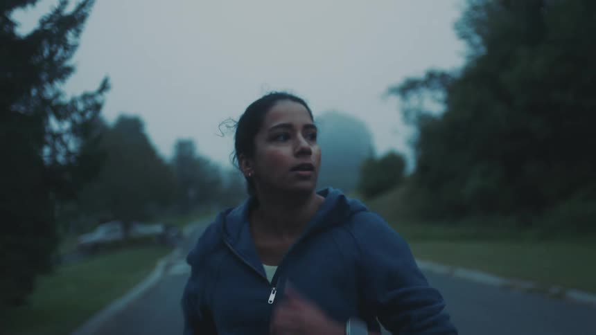 A woman jogging on an empty street surrounded by trees on a misty morning