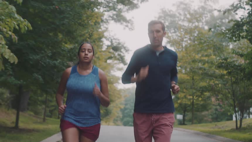 Woman and man running together in a park with trees around