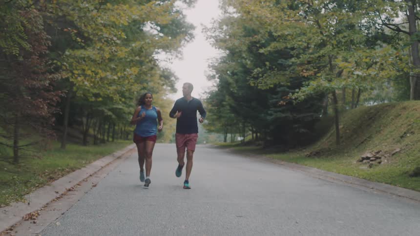 Man and woman running on a road surrounded by trees