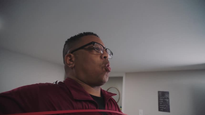 Man stands in room breathing while exercising with exercise bands