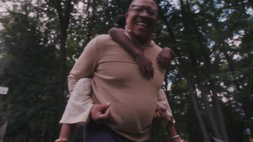 A father gives her daughter a piggy back ride in the park