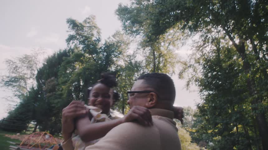 Girl running on her fathers lap in a garden with trees