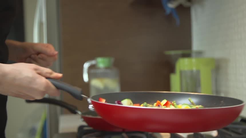 A person cooks vegetables in a pan