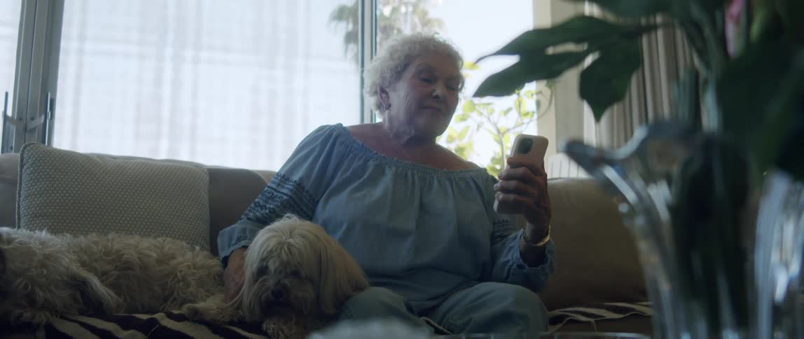 An elderly woman reading on her smartphone sitting on the couch at home with her dog