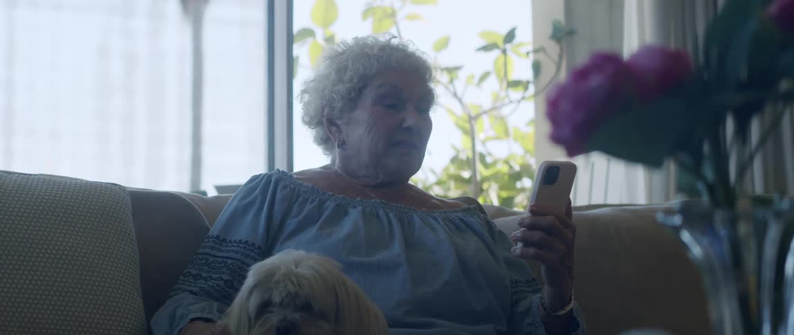 Elderly woman sitting interacting with her smartphone while petting a dog next to her