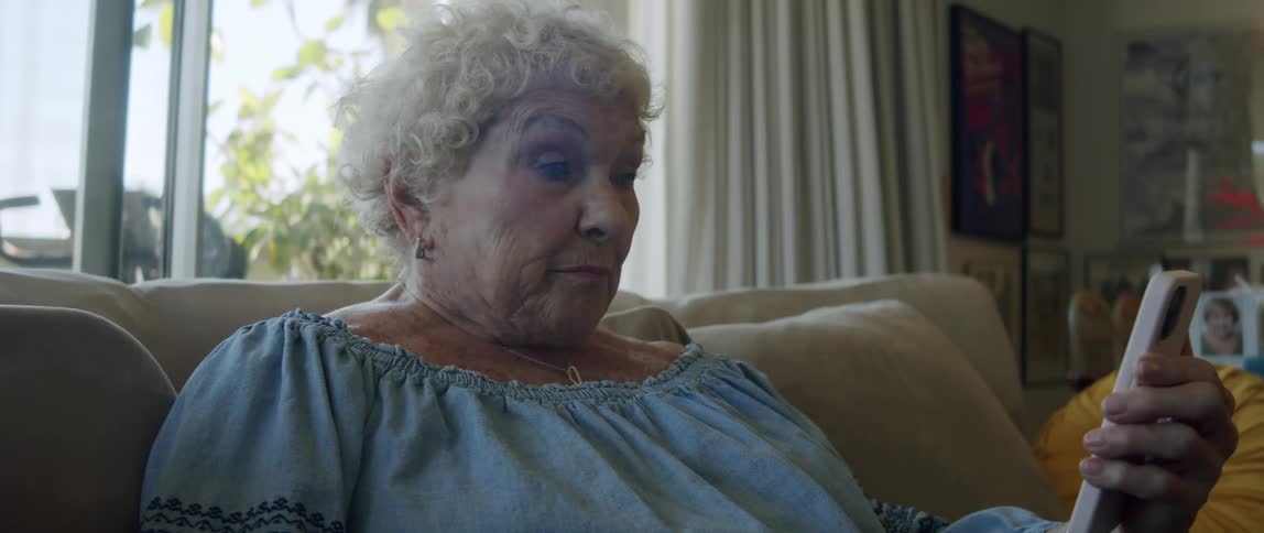 Elderly lady sitting in living room and being surprised while looking at her smartphone