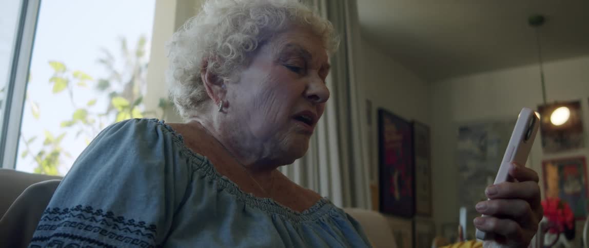 An elderly woman reading on her smartphone sitting on the couch at home