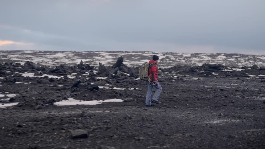 Man with backpack walking through a natural area towards a parked vehicle