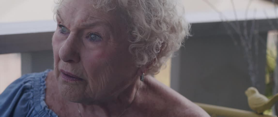 An elderly woman reading the newspaper gets suddenly surprised and sad