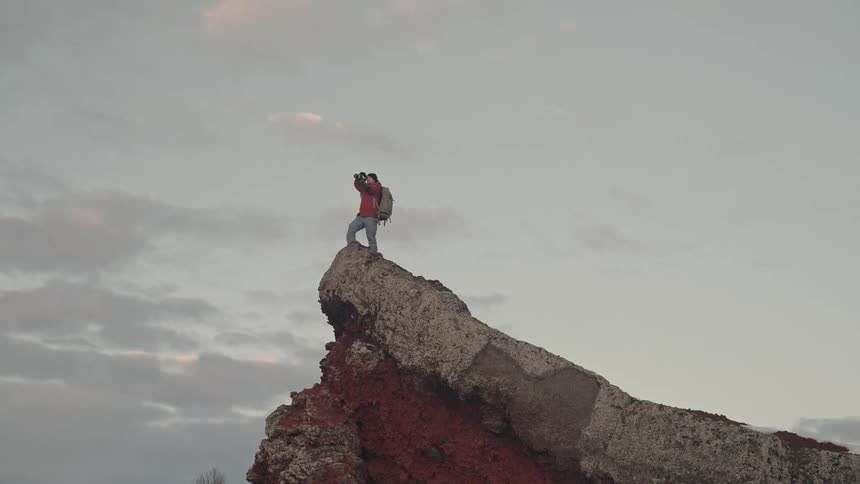 A person stands on a mountain summit taking photographs with a camera