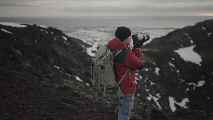 A photographer takes pictures of a barren snow covered mountain range