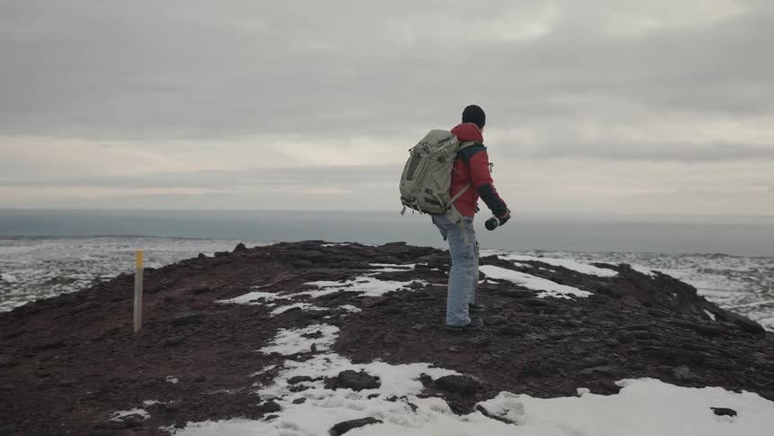 Man walking on a snowy mountain by the sea on a cloudy day