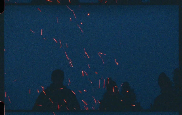 Silhouette of a group of people standing in front of a campfire with sparks flying in the air