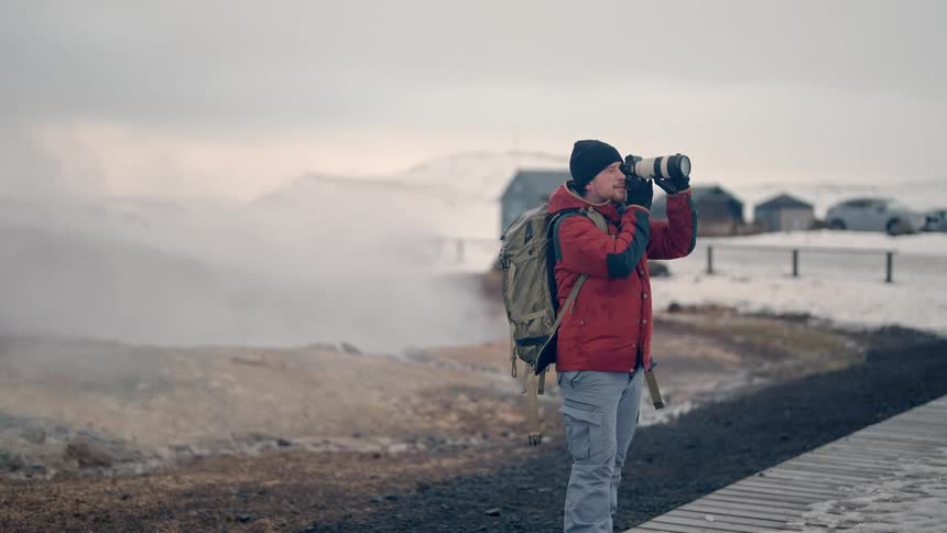 Male hiker uses a telephoto lens to take a picture while standing on a path in a rural town on a foggy winter day