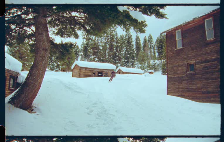 A skier moves down a snow covered hill inbetween wooden buildings