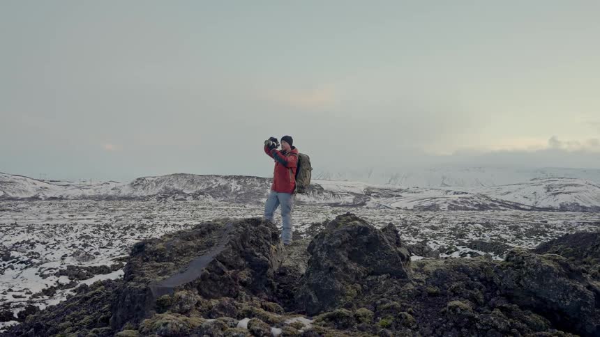 Man standing on rocky terrain using a camera with a professional lens