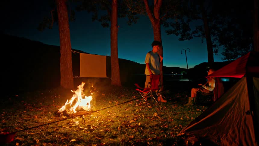One brother high fives his younger brother at a campsite with a blazing fire
