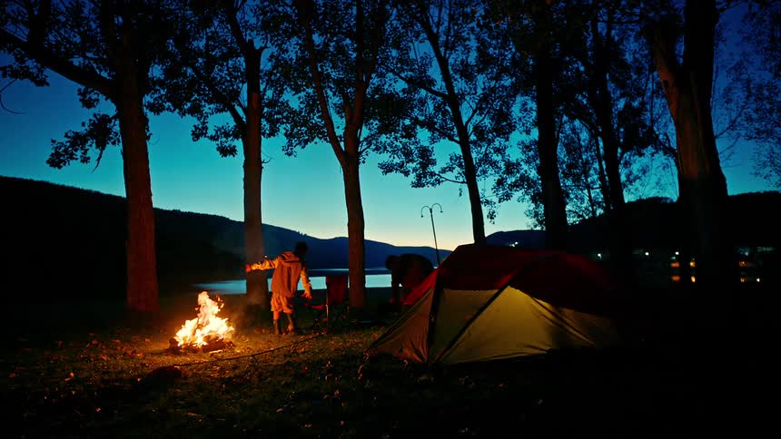 Two boys sitting on a chair next to a tent in front of a campfire at a campsite