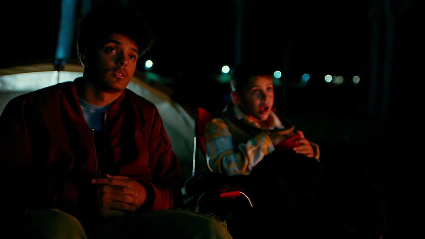 Two boys sitting eating and talking while camping at night