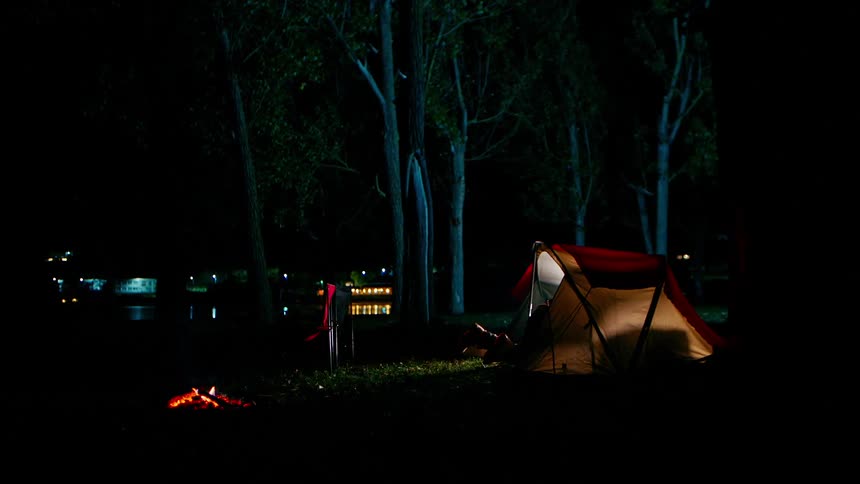 Man lying in a tent by a lake and turning off the light