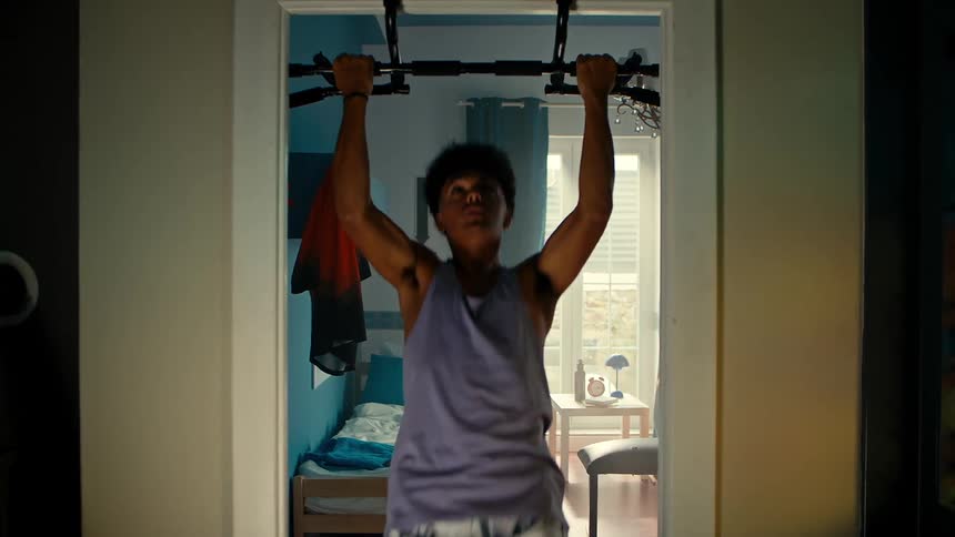 A teenage boy does pull up exercises in his bedroom doorway