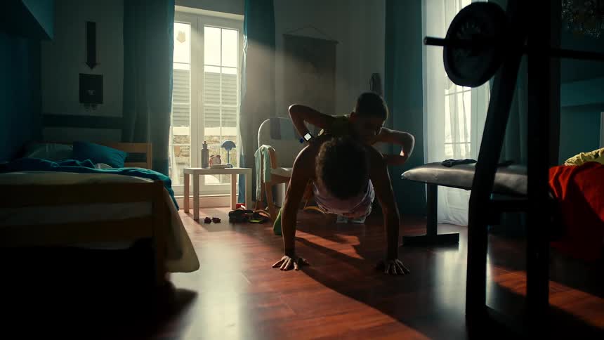 Younger brother stops doing arm curls to jump on the back of an older brother doing push ups