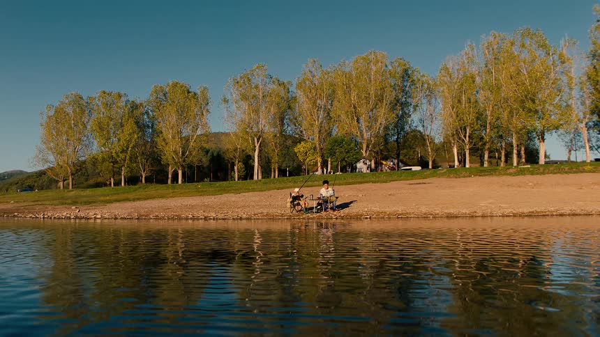 Two people sitting on the bank of a river fishing