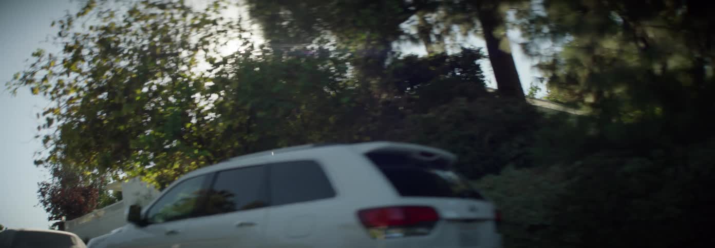 Cars and vans sit parked on the side of a road next a forest