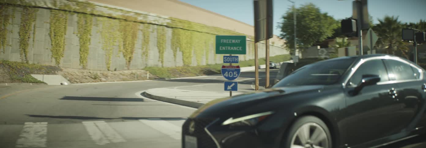 A sleek black sedan navigates a winding road leading to the freeway entrance under the clear blue sky
