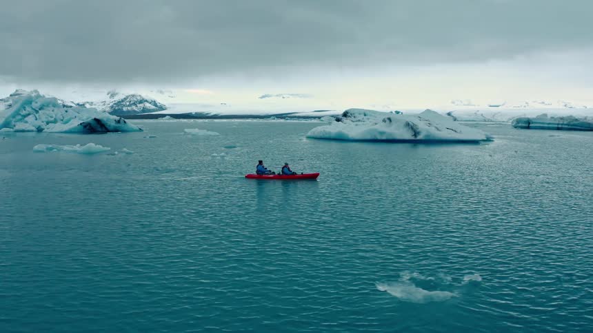 Two people row a canoe around large icebergs near a coastal area