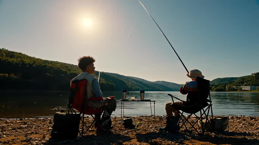 Two young men sitting on the shore of a lake fishing