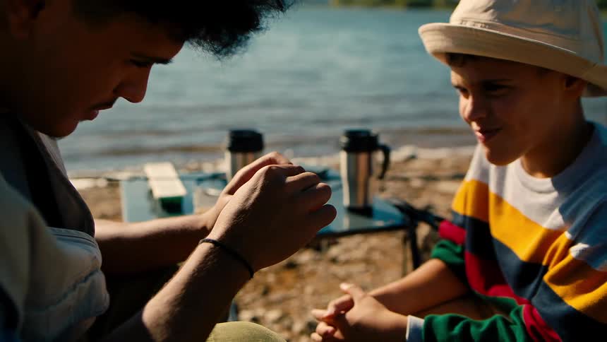 Teenage girl and a boy sitting watching a fishing lure by a lake