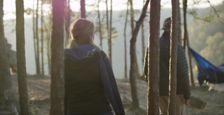 Couple and their dog walking through trees towards a couple of hammocks at sunset
