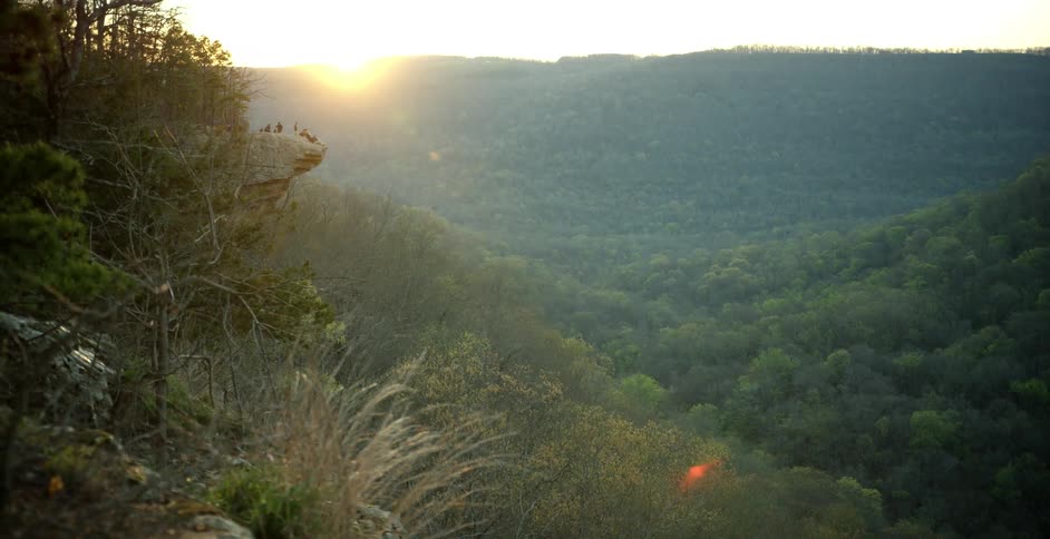 Sun setting behind a tree covered mountain