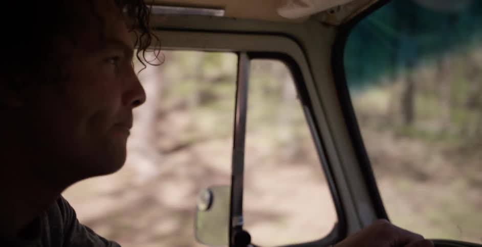 A man driving a vehicle with many trees on the side of the road