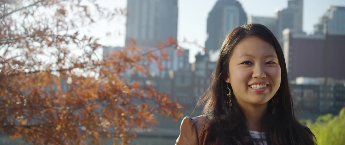 A young woman smiles in front of a city skyline on a sunny day