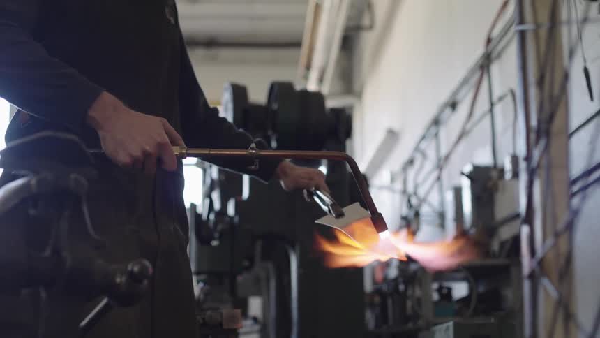 Blacksmith using a blowtorch directly on a blade and heating it