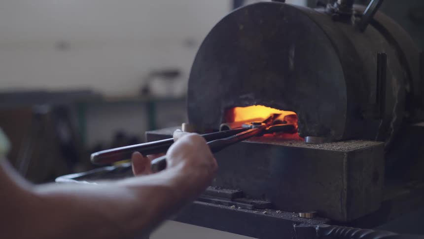 Person holding a tool and forging a mental on a welding plate